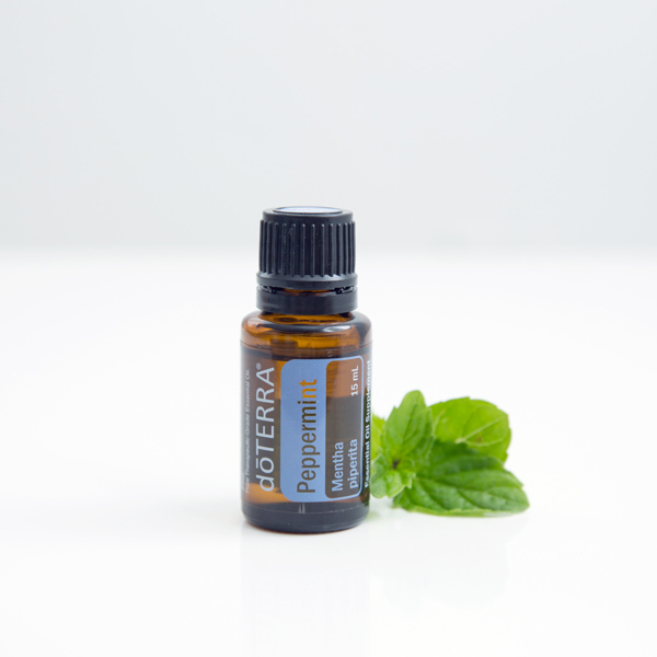 Флакон Мята перечная dōTERRA рядом с зелёными листьями