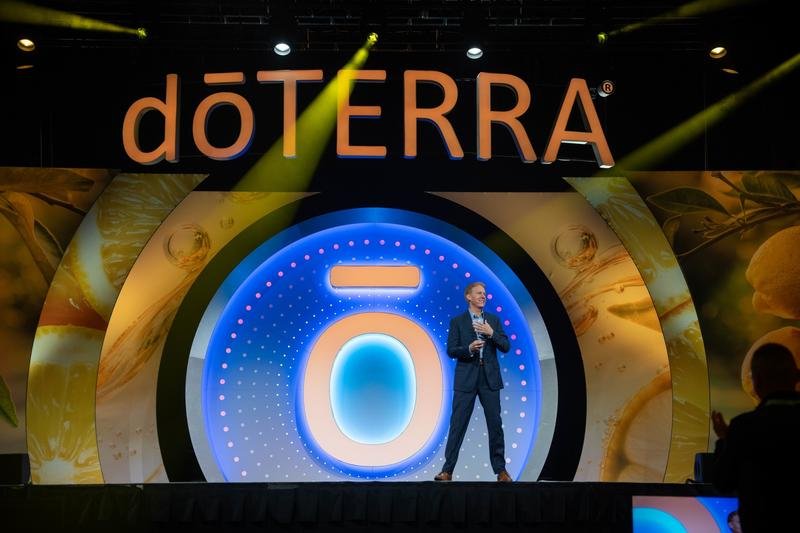 Дэвид Стирлинг на большой сцене под логотипом dōTERRA в лучах прожекторов